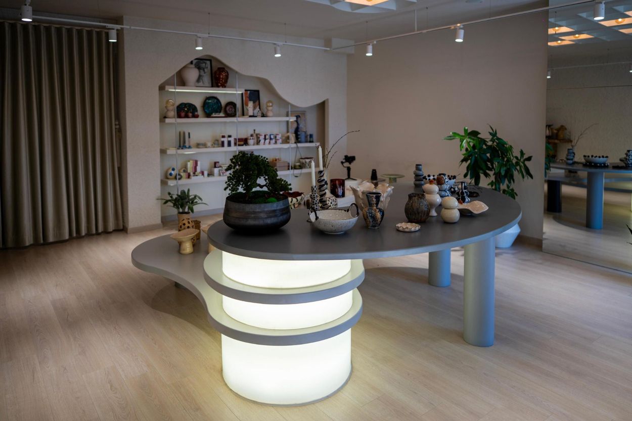Showroom genel görünümü — merkezde ışıklı gövdesiyle Fasulye Masa ve dalgalı raf nişi